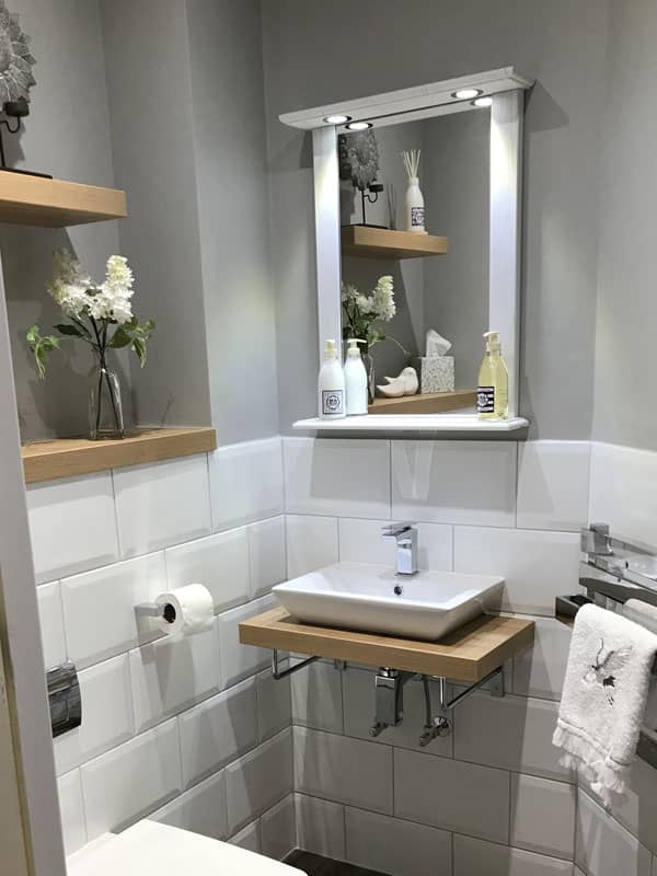 White floating sink with grey walls and white tiles and a light up mirror